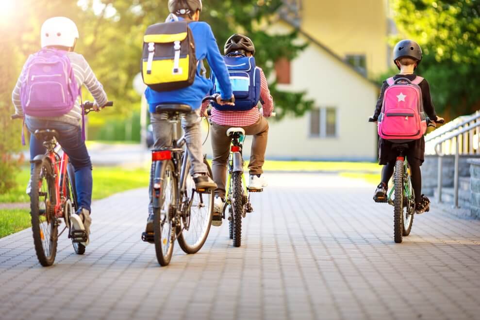 A group of kids bikes to school on a sunny day, wearing backpacks.