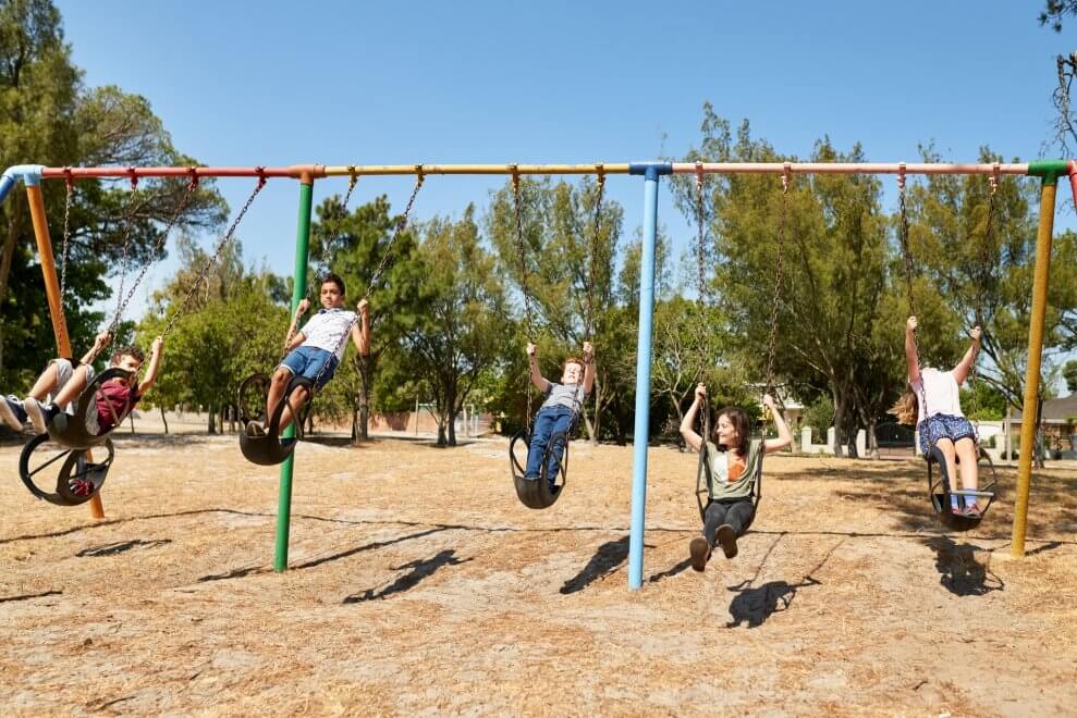 Five children swing on playground swings on a sunny day.