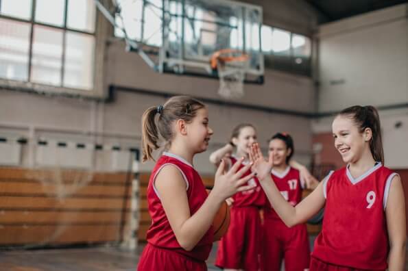 Two girls on the same basketball team high-five on the court.