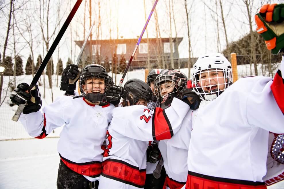 A group of kids dressed in hockey uniforms cheer as they play on an outdoor rink.