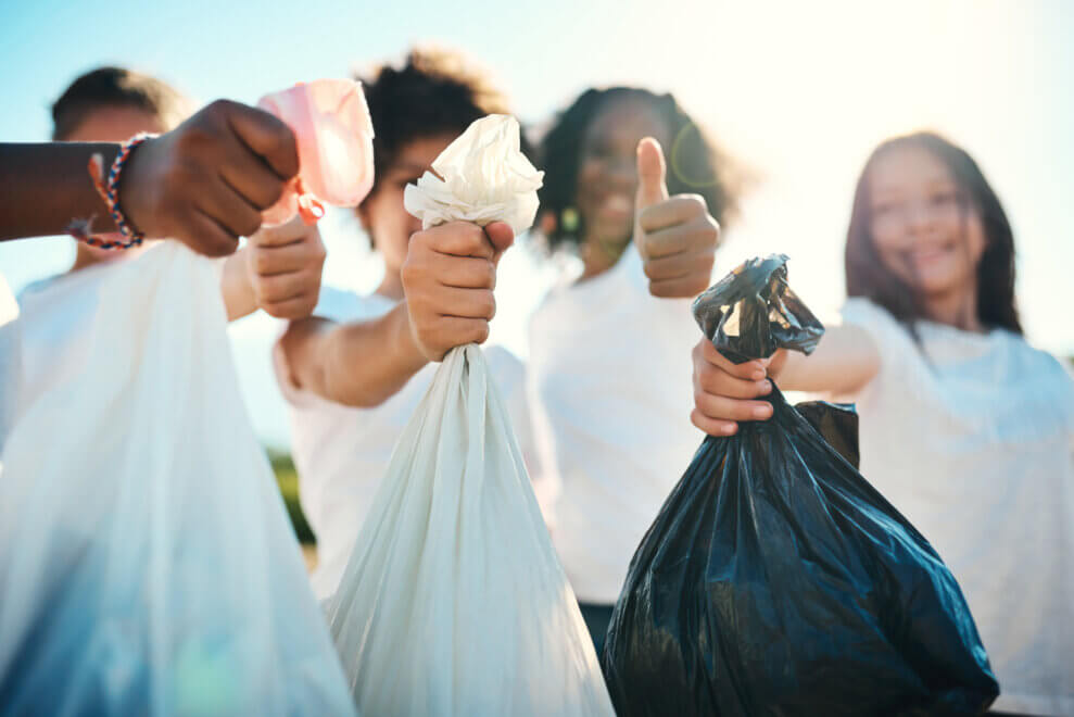 A group of kids hold up garbage bags full of litter. One girl smiles and gives a thumbs-up.