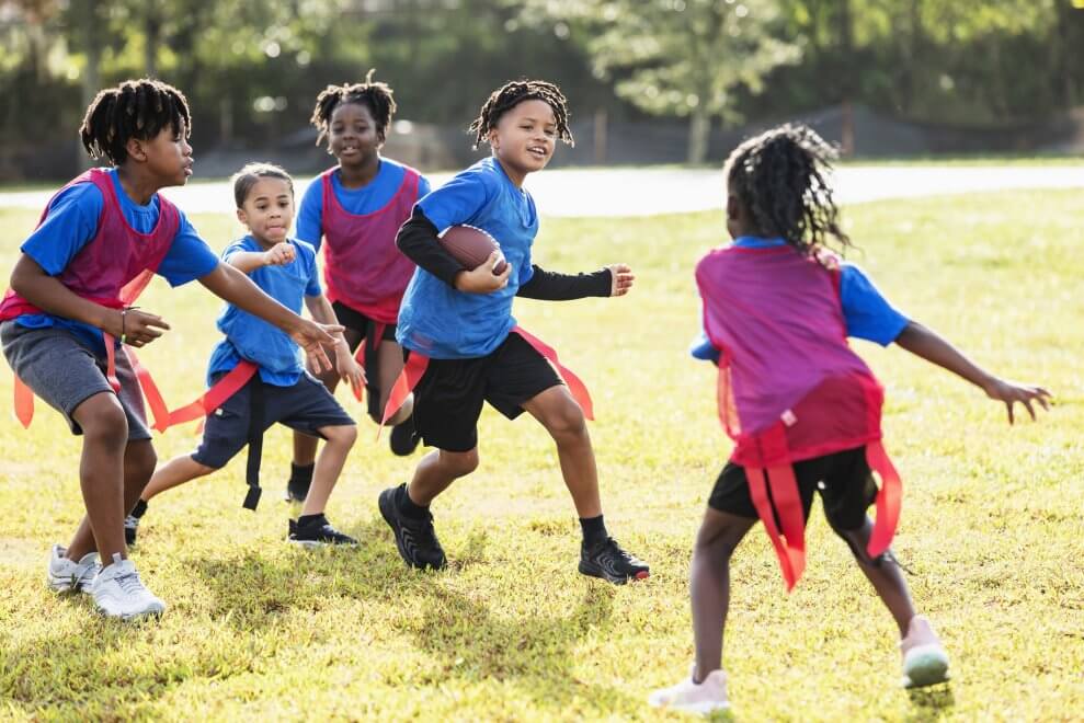 A group of kids plays flag football on a sunny day on a grassy field.