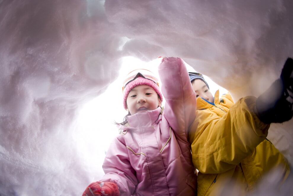A sister and brother dig a hole in the snow.