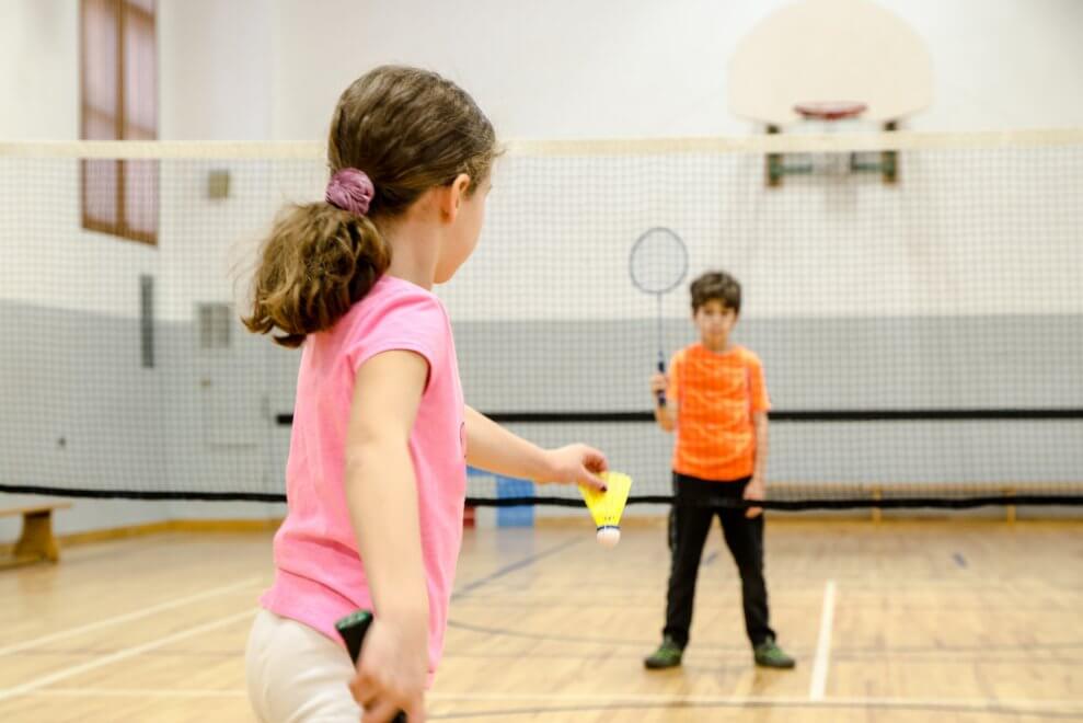 A young girl prepares to serve a badminton birdie over the net to the boy she's playing against.