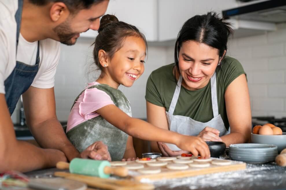 A girl bakes cookies in the kitchen with her mom and dad. 