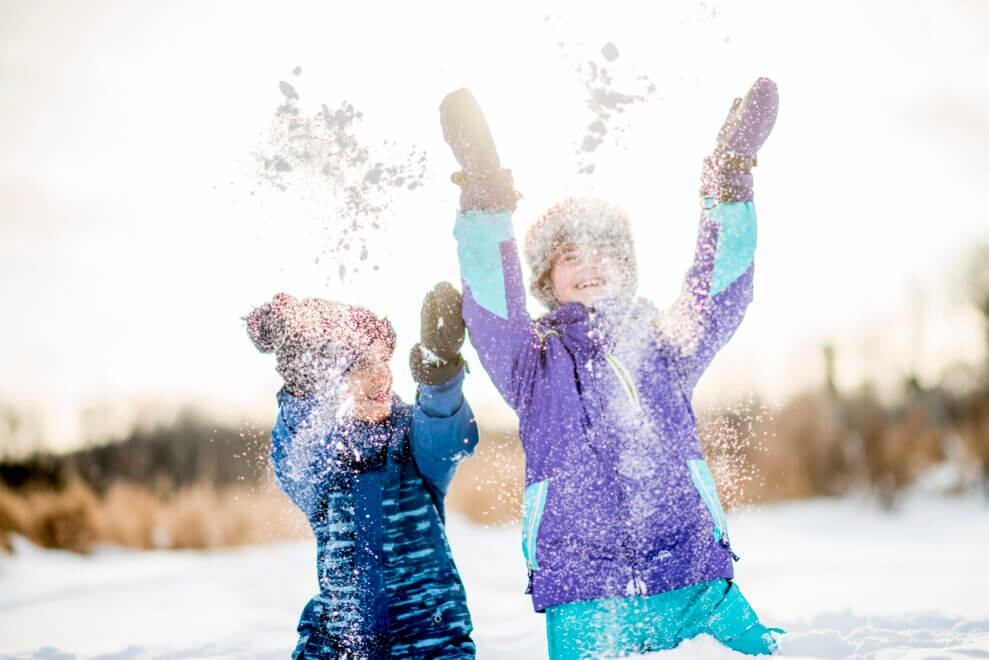 Brother and sister throwing snow into the air and laughing