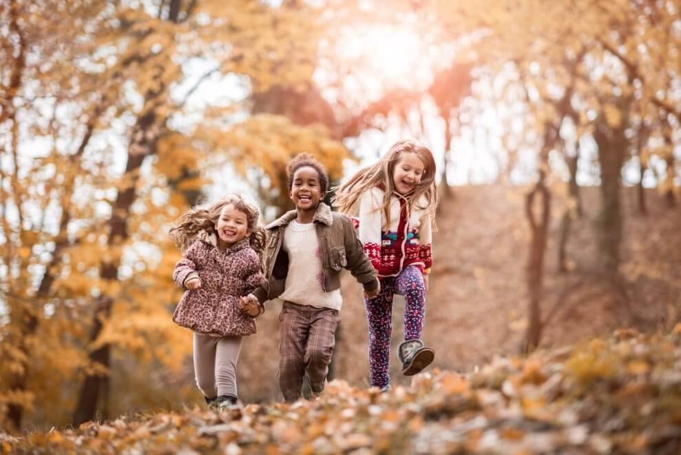 Three girls run and laugh outside on a fall day.