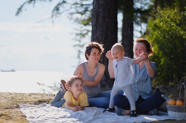 Two moms and their two young children have a picnic near the ocean on a sunny day.
