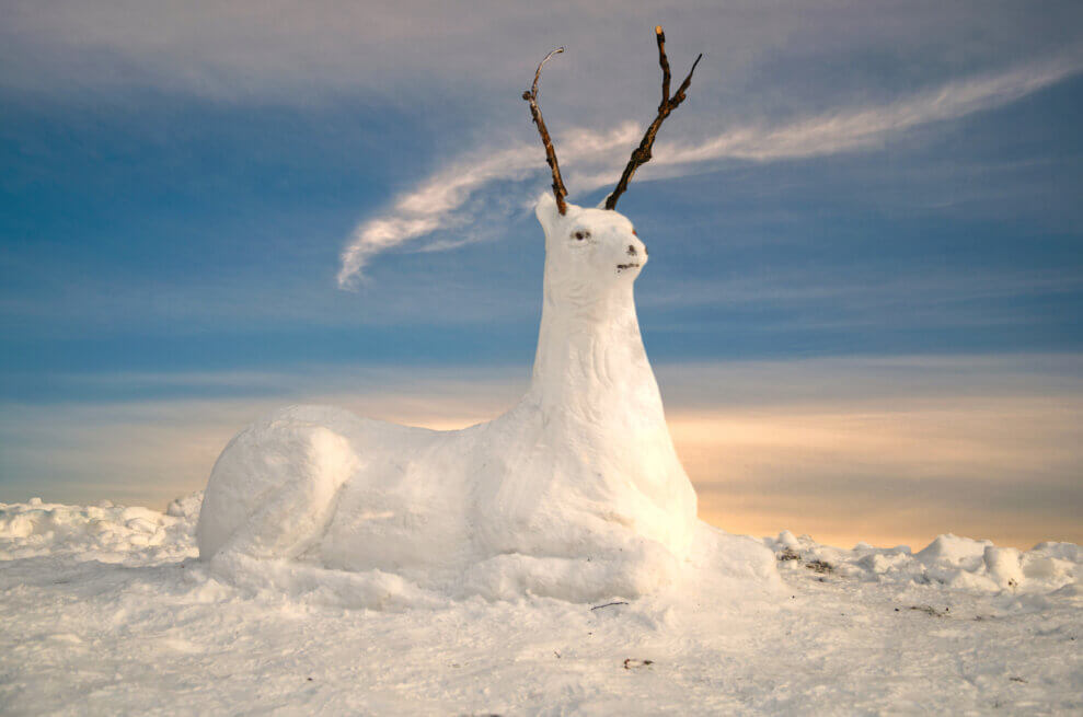 A snow sculpture in the shape of a deer, with sticks for antlers