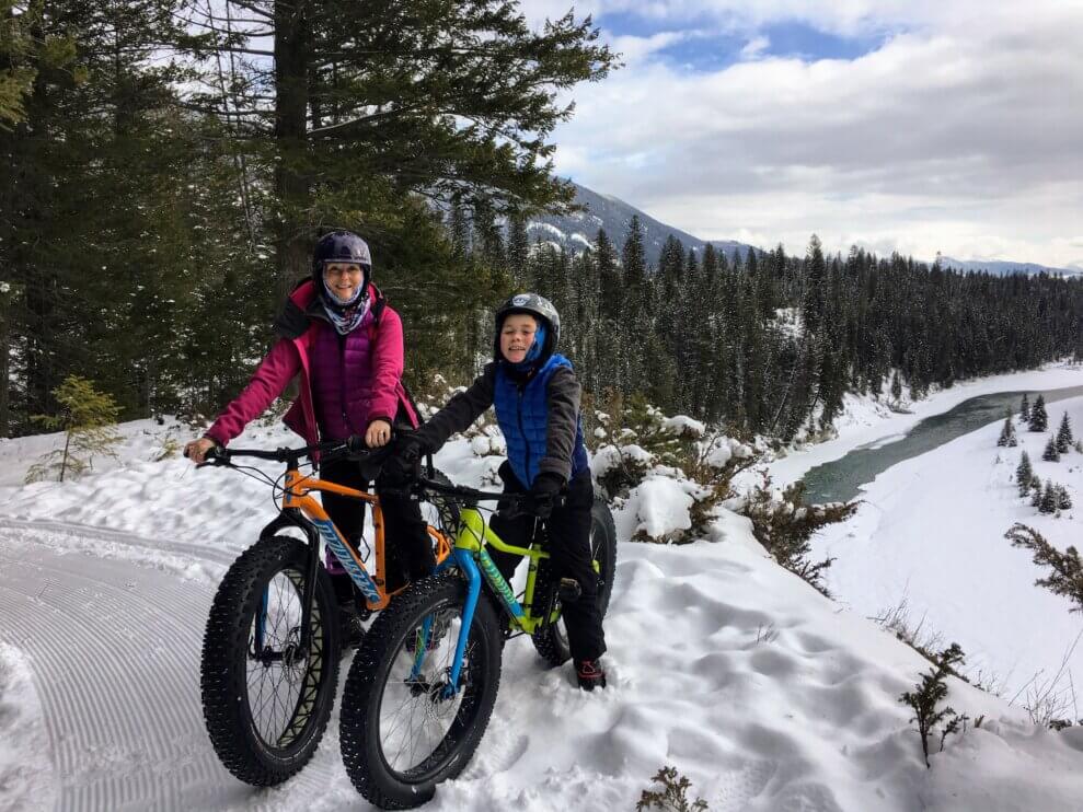 Mom and son sit on fat bikes in the forest, smiling 