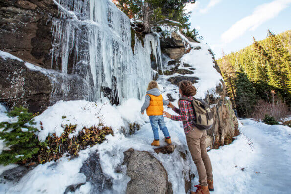 Mother and child standing in the forest looking up at a frozen waterfall