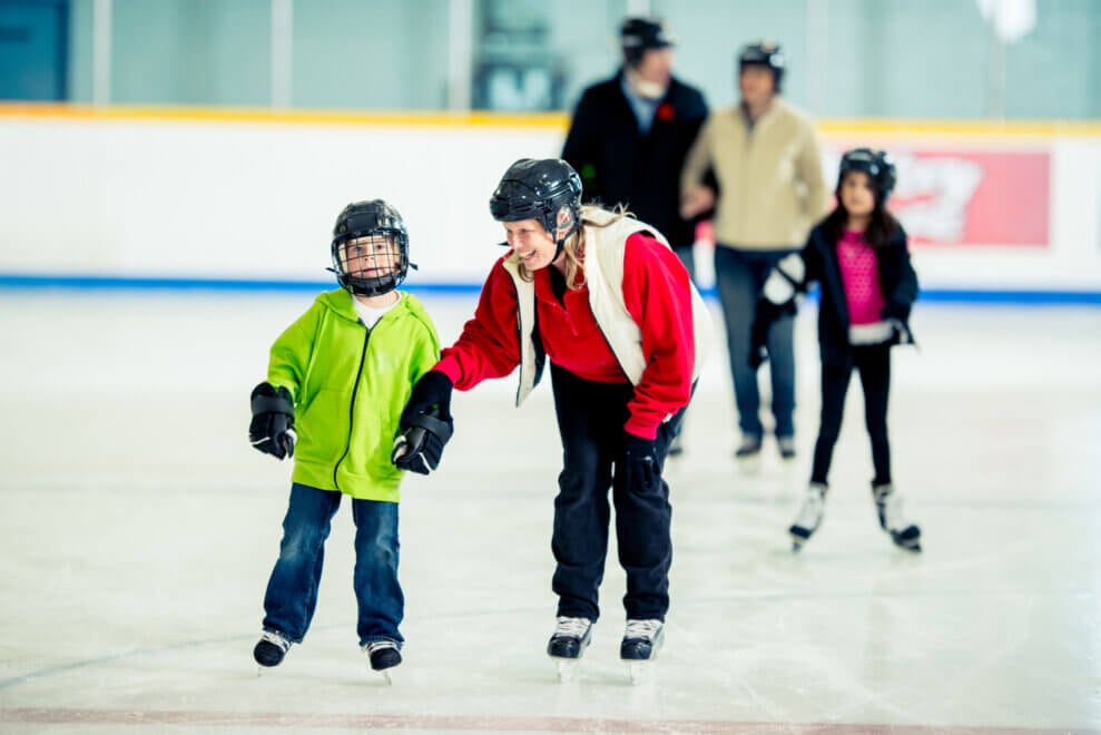 Mother and son skate on an indoor rink while holding hands