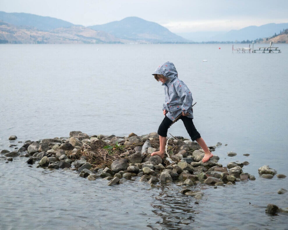 Child walks on a pile of rocks along the shore of a body of water
