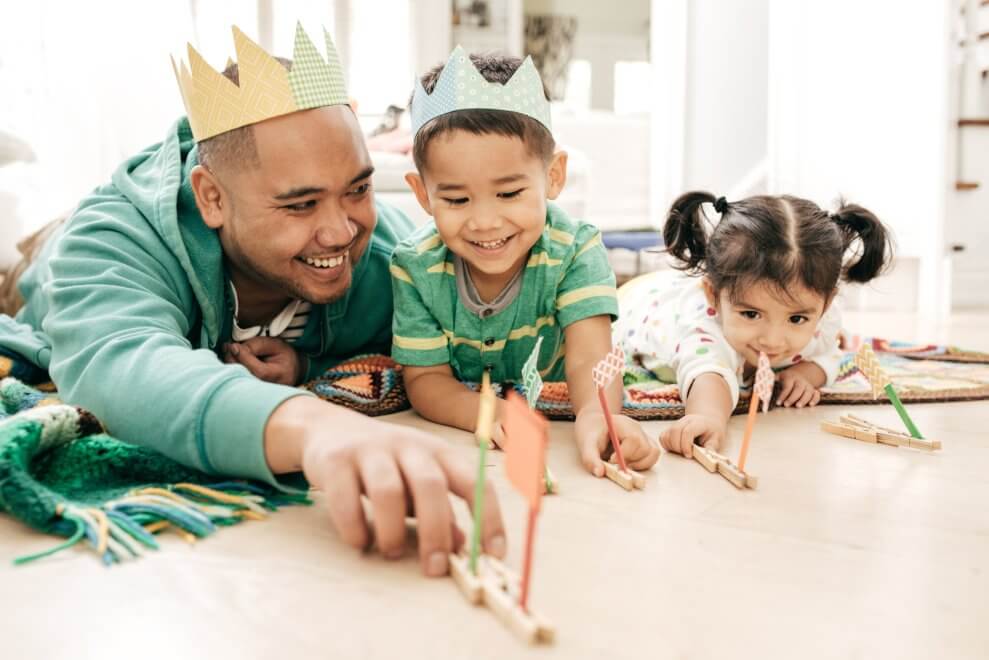A dad plays with his two young children on the living-room floor.