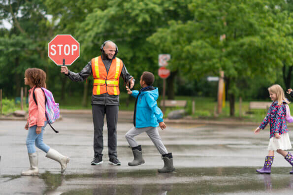 Kids walk across the street in front of smiling crossing guard