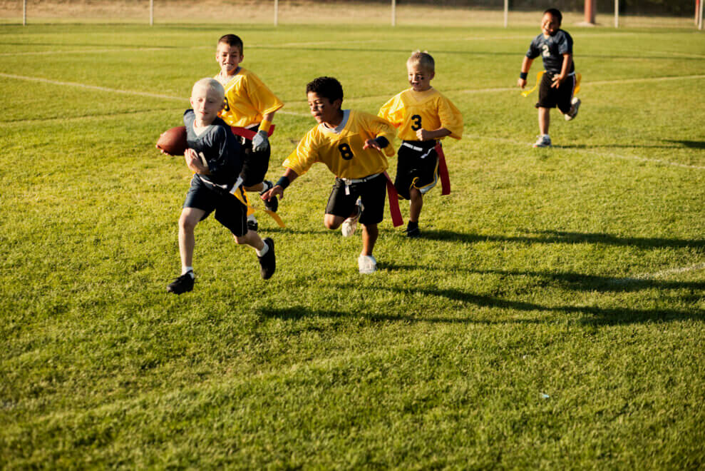 A group of boys plays flag football outdoors on a grass field
