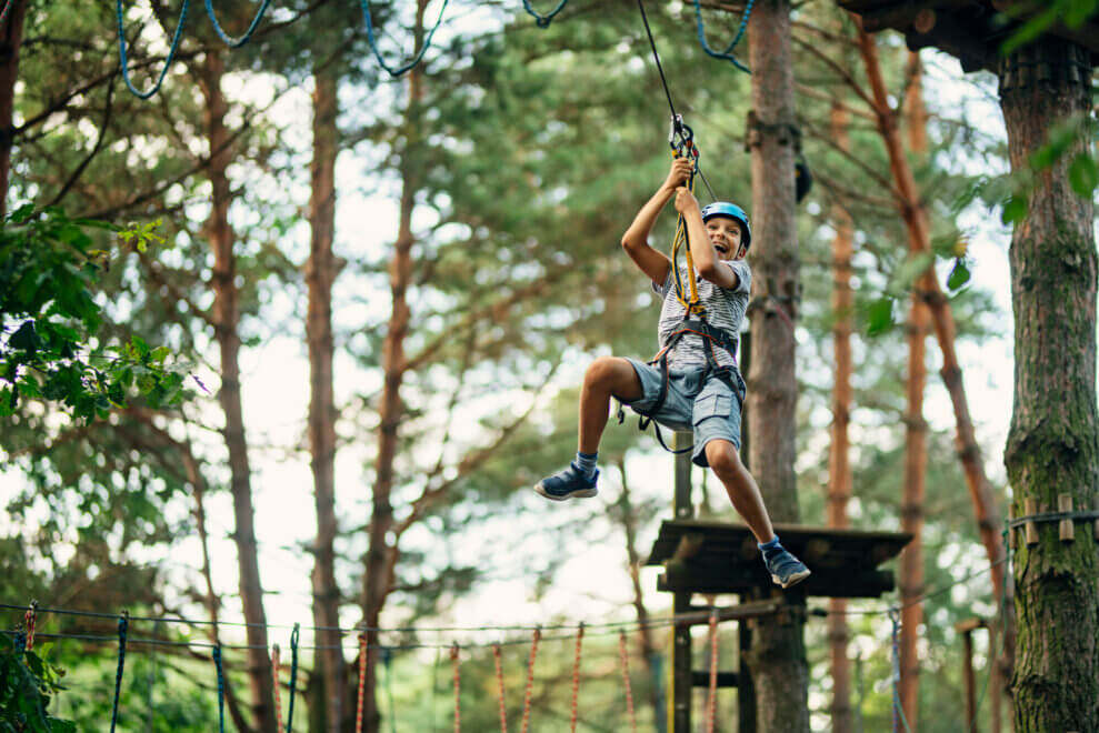 Boy ziplines through forest with a big smile on his face