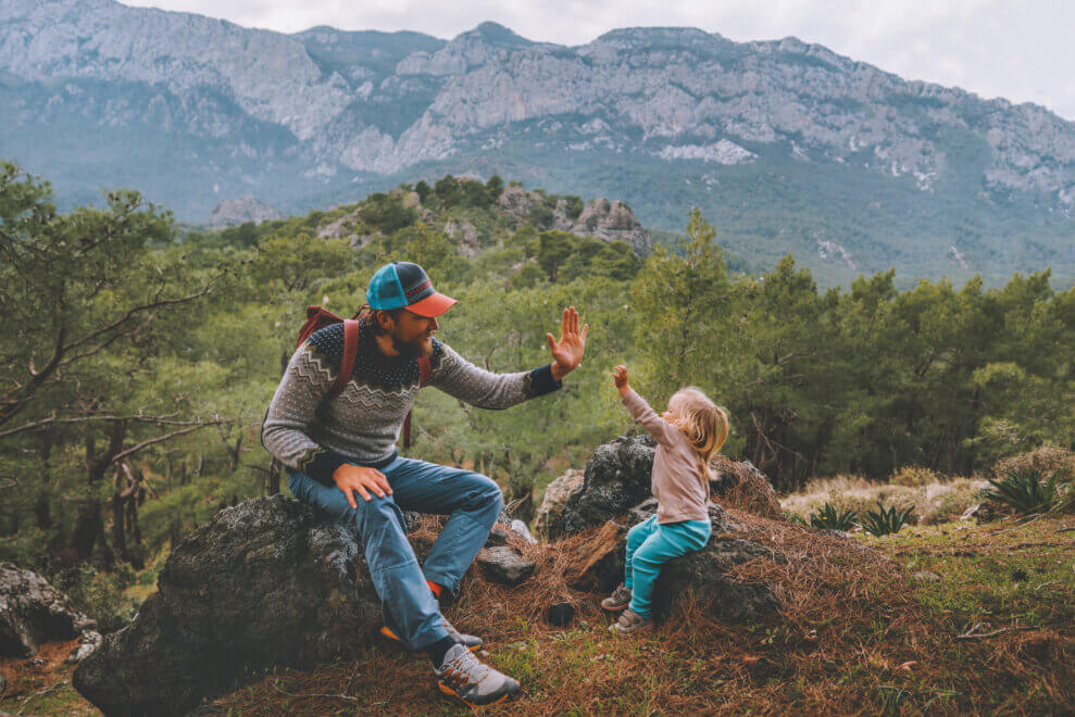 Father and toddler daughter sit at a lookout, high-fiving