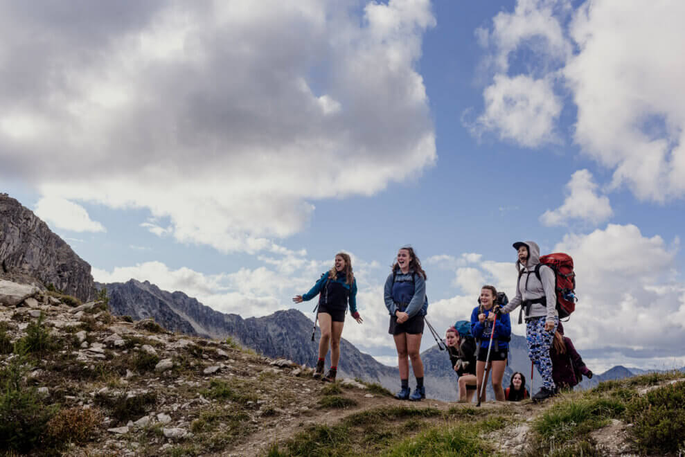 Group of teen girls hike into the alpine, exclaiming about the beautiful scenery around them