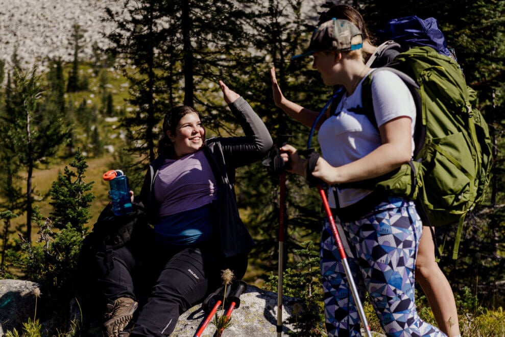 Two girls high-five on the side of a forested trail