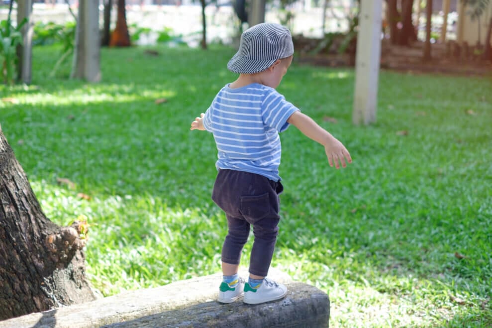 Toddler balancing on a stone beam in a grassy park