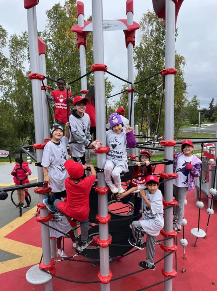 A group of children climb and hang out on a climbing tower. They're wearing Jumpstart T-shirts.