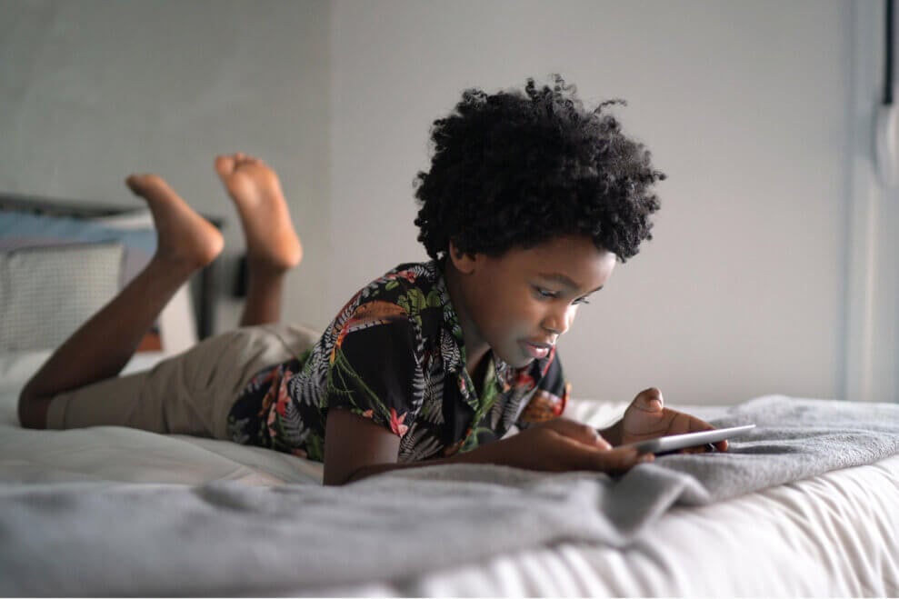 Boy lies on a bed on his stomach, using an iPad