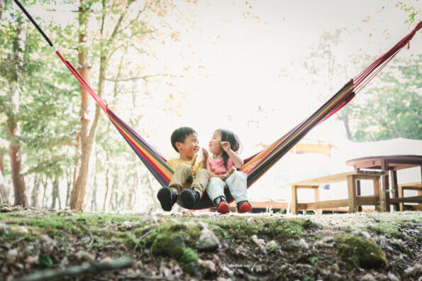 Brother and sister sit on a hammock, smiling at each other