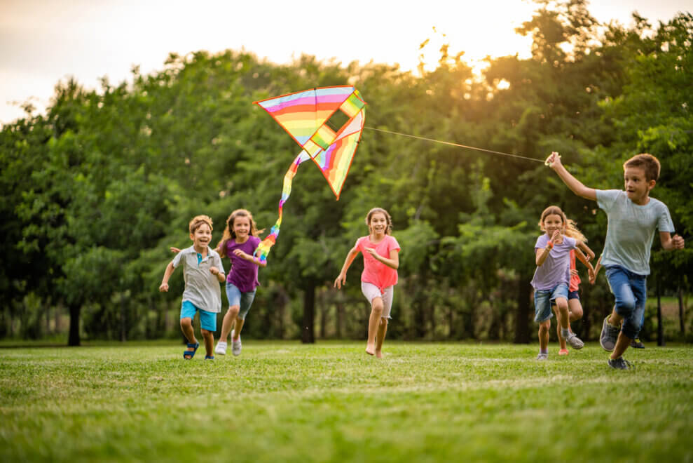 Group of happy children in the park, chasing one boy who's flying a kite