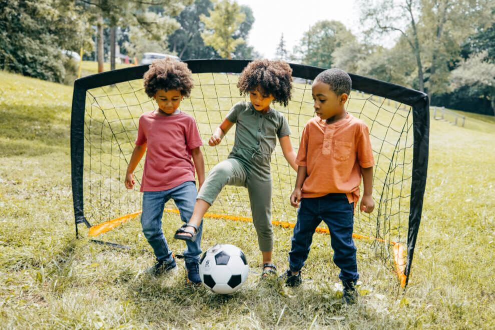 Three kids kicking a soccer ball around in the park
