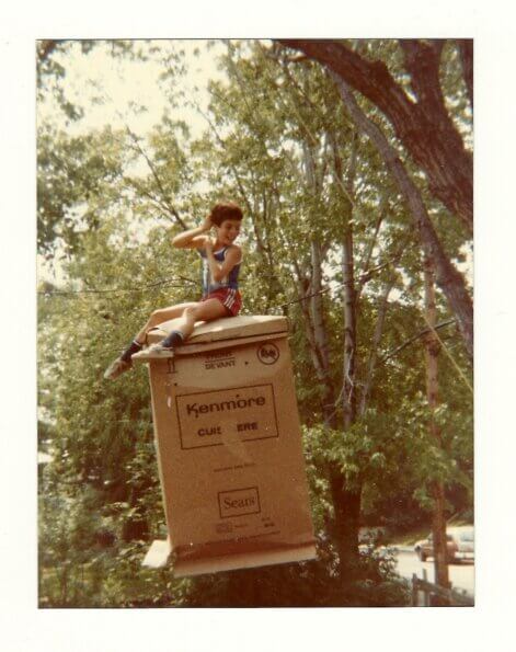 With a smile on his face, the author's brother swings on an empty fridge box hanging from a tree in their childhood yard.