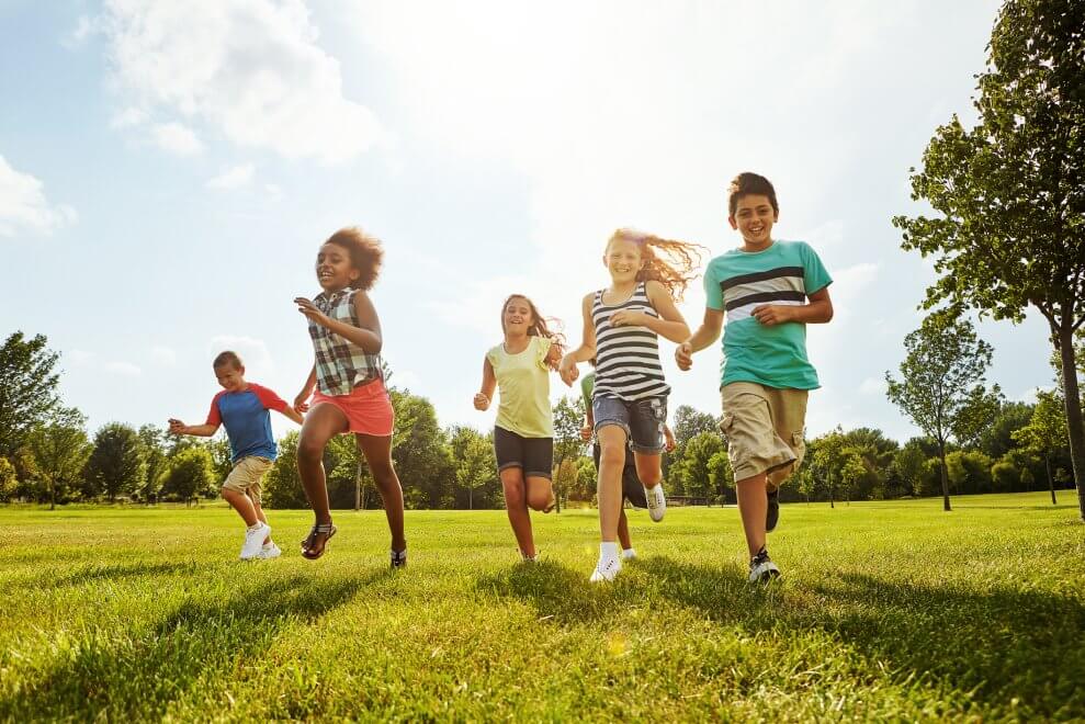 A group of elementary-age kids run across a field on a sunny summer day.
