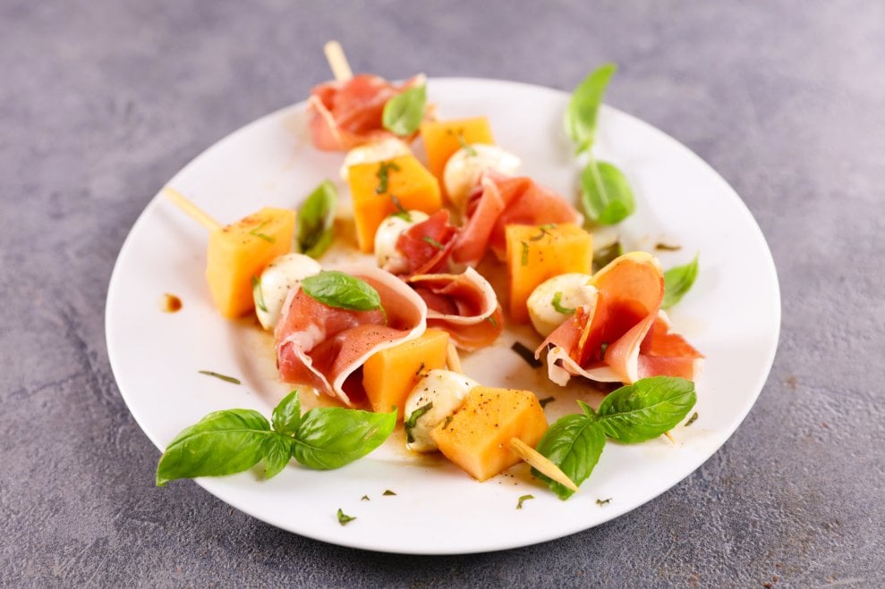 Melon and prosciutto skewers, garnished with basil leaves.