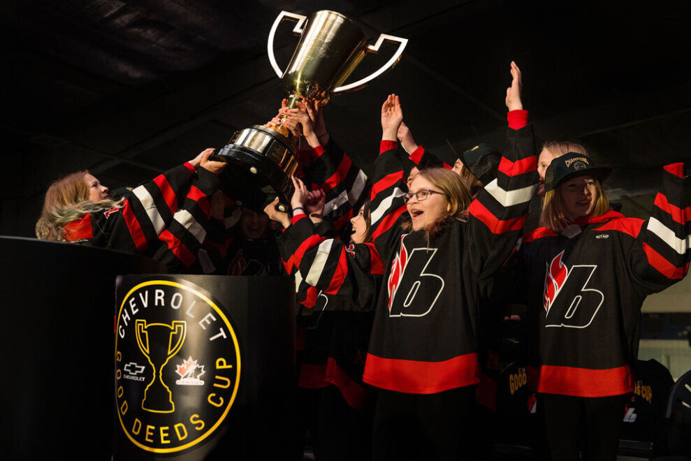 A group of smiling girls wearing their hockey jerseys hoists the Chevrolet Good Deed Cup over their heads as part of the Canadian challenge that aims to inspire youth to do good in their communities.