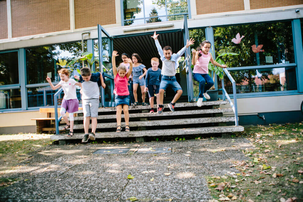A group of students run out of school into the playground for recess