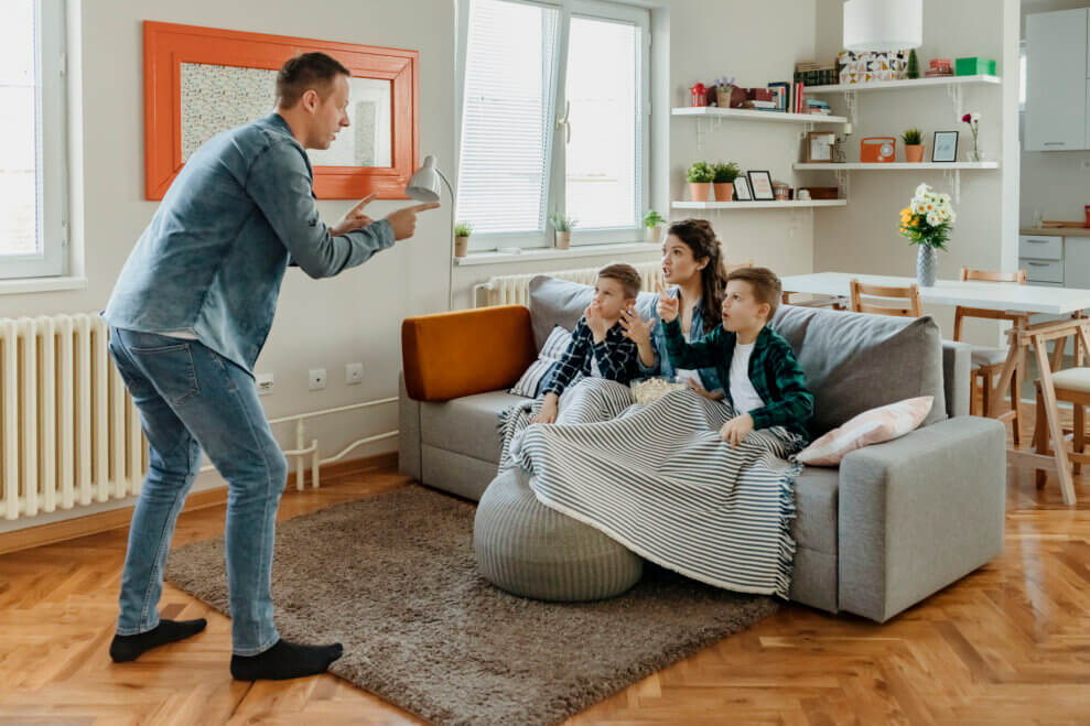 A father, mother, and two sons play charades in their living room at home.