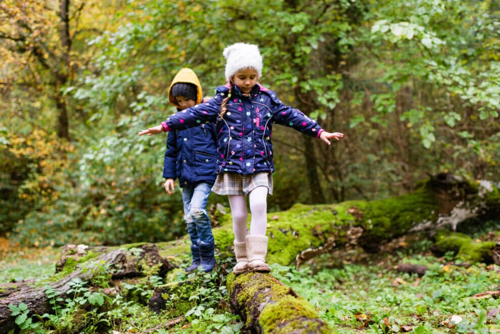 Two siblings walk along a log as part of an active scavenger hunt.