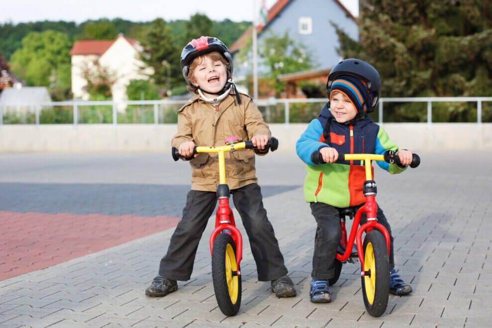 Two toddler brothers sit on their balance bikes.