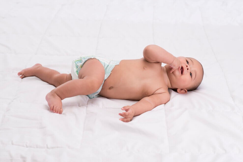 A baby lies on his back and starts to roll over onto his stomach.