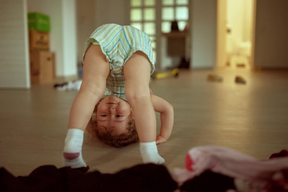 Toddler rests her head on the floor and looks at her feet, in a movement similar to downward dog. 