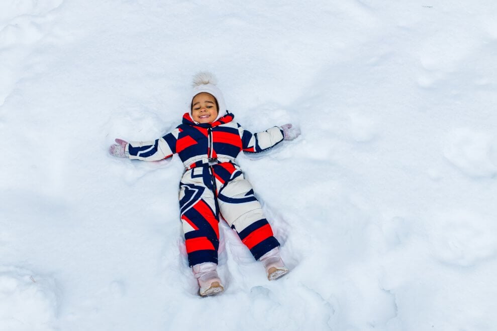 A little girl wearing a snowsuit makes a snow angel.