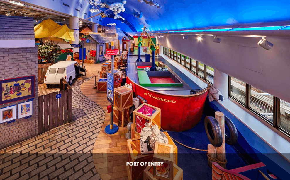 Photo de l'aire de jeu de l'entrée du port au Musée canadien des enfants, avec un bateau, des caisses, un mur et un sol peints en bleu.