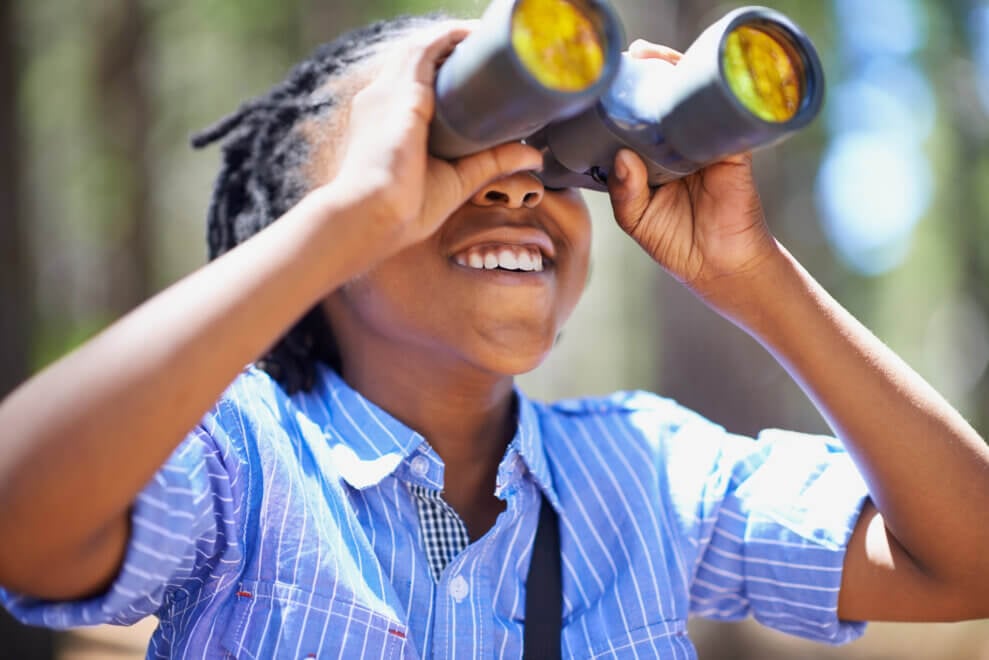 A child looks through binoculars with a smile on their face.