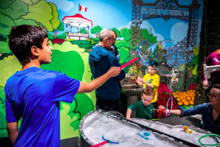 A boy waves a wand at the Discovery Centre and large bubbles emerge from it.