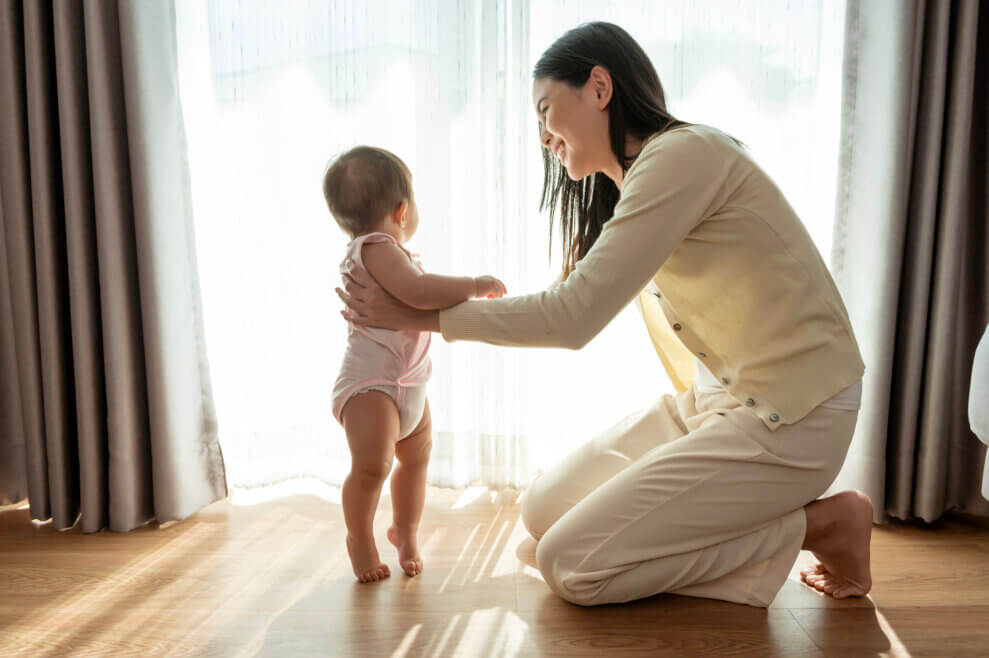 A mother supports her baby in a standing position.