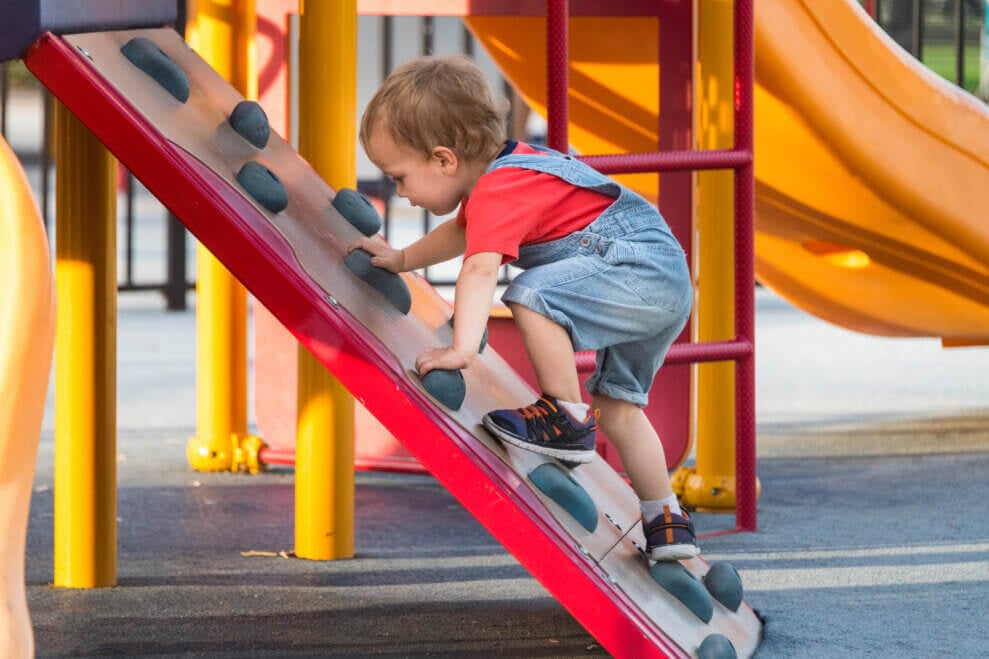 A toddler climbs up a kids' rock-climbing slope at a playground.