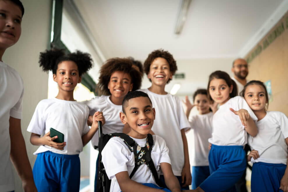 A group of preteens stands together in a hallway. One boy uses a wheelchair. 