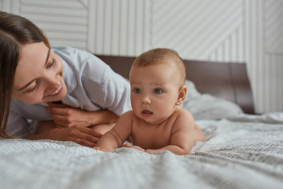 A baby lies on their stomach while their mother lies next to them, with a smile on her face.