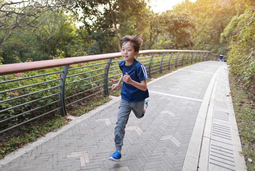 A boy runs on a walkway through a park on a sunny evening.