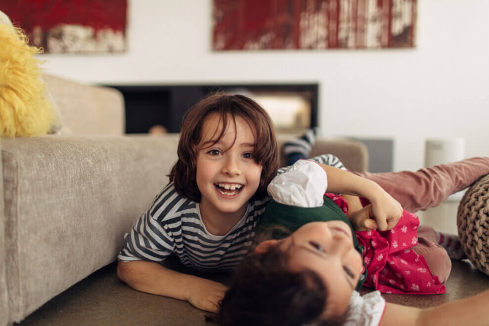 Two siblings wrestle and laugh on the living-room floor.